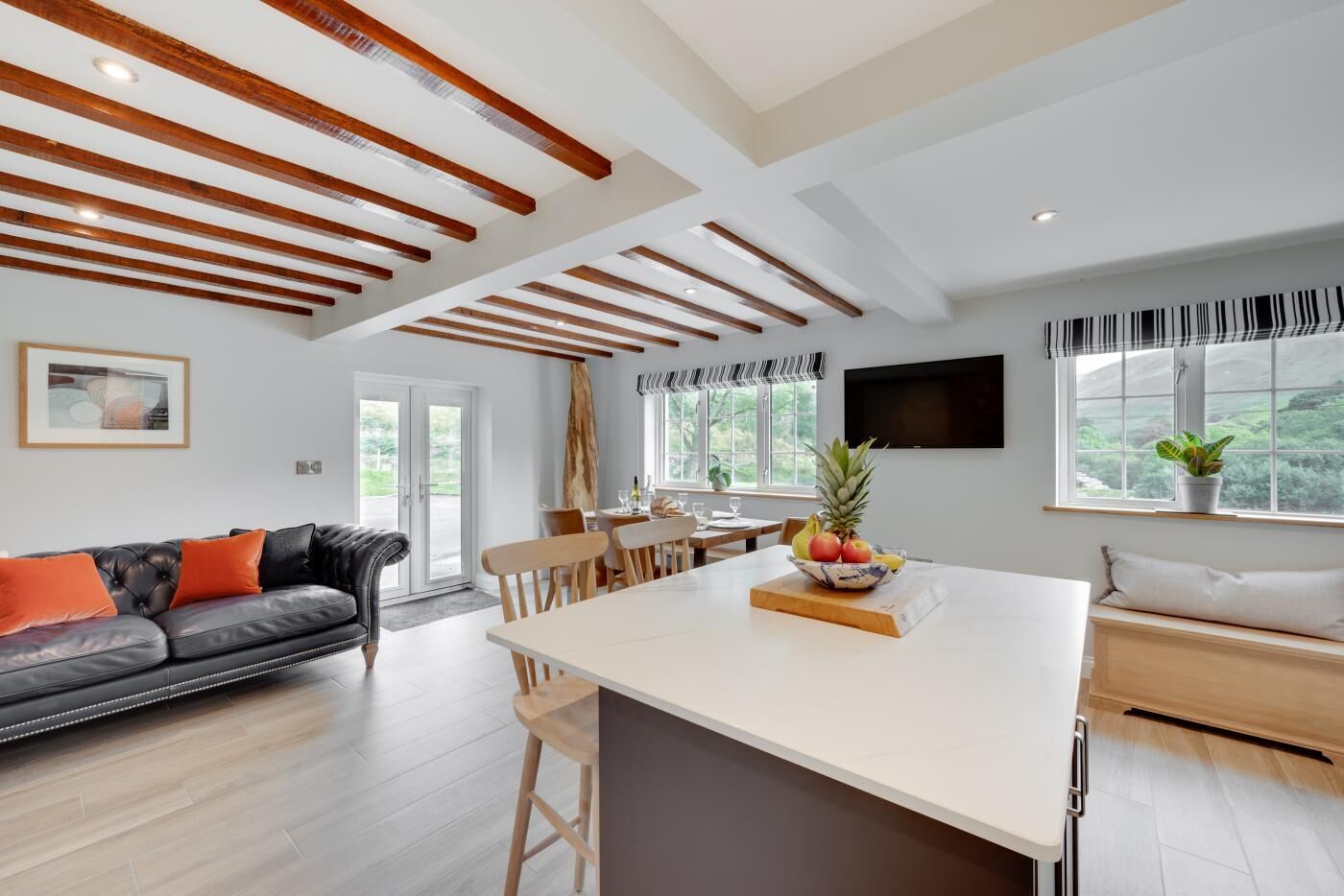 A modern kitchen with a central island, wooden beams on the ceiling, and a dining area with a table and chairs.