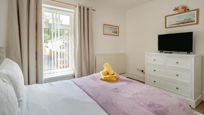 Quarto com cama, televisão, cómoda, janela com cortinas e radiador.