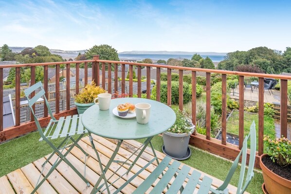 A balcony with a table, chairs, and potted plants.