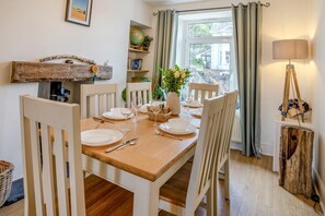 A dining area with a wooden table set for four, white chairs, a globe, books, and a lamp.