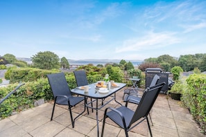 A patio with a table set for two, surrounded by chairs, overlooking a scenic view.