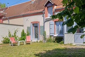 Ein Haus mit Ziegeldach, Backsteinfassade und einem kleinen Vorgarten mit zwei Stühlen und einem Tisch.
