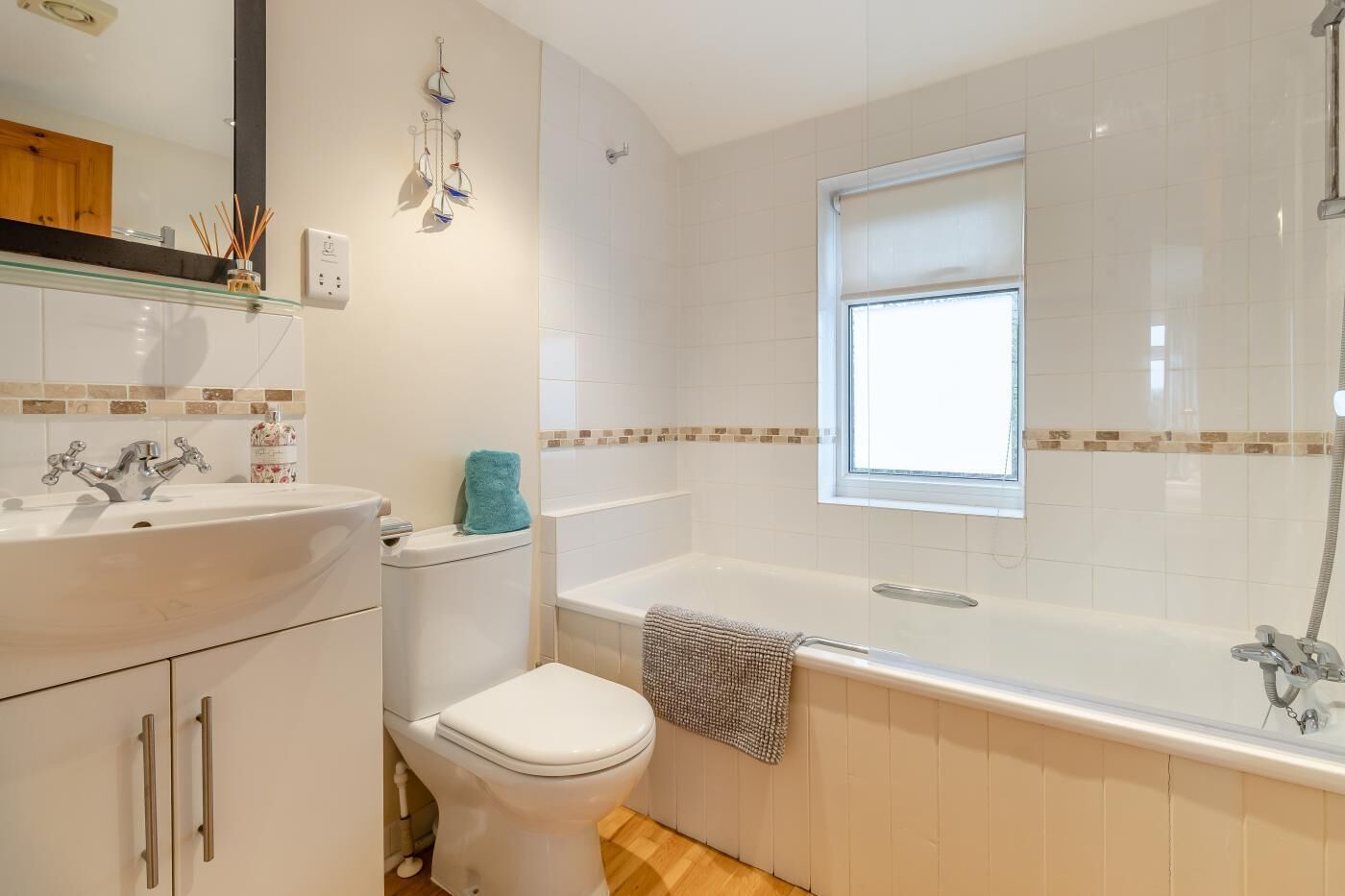 Ein modernes Badezimmer mit einem weißen Waschbecken, einer Toilette und einer Badewanne. Über der Badewanne befindet sich ein Fenster und über dem Waschbecken ein Spiegel.