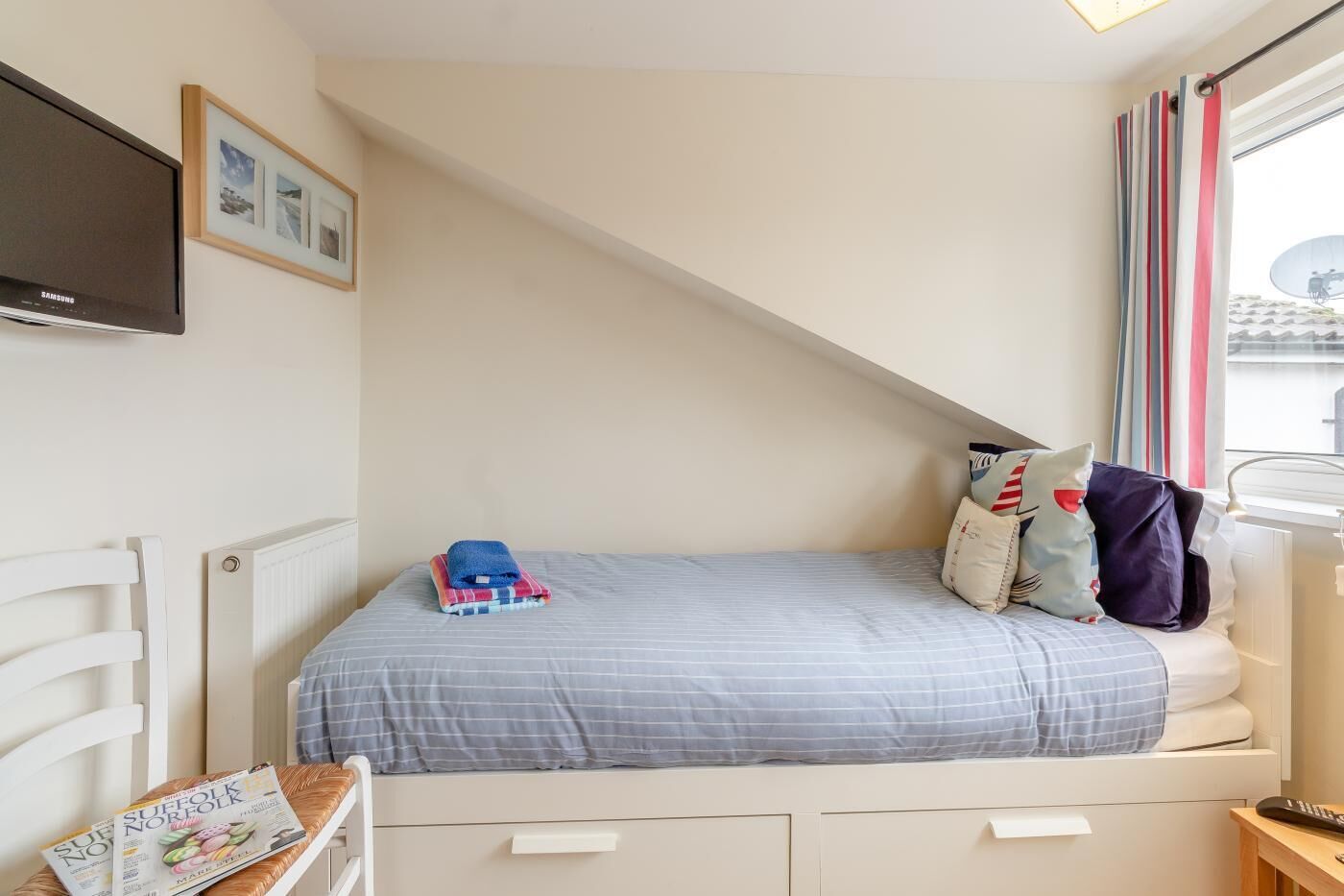 Een slaapkamer met een bed, een aan de muur bevestigde televisie, een raam met gordijnen en een radiator.