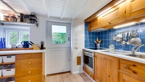 A kitchen with wooden cabinets, a white countertop, and a blue backsplash. There is a window with a view of greenery outside.