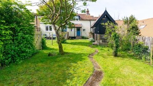 A well-maintained garden with a gravel path leading to a house with a tiled roof and a blue door.