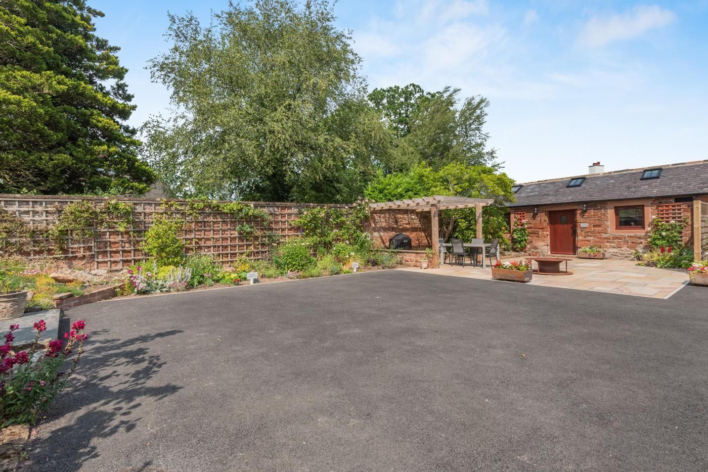 A courtyard with a paved area, a stone wall, a brick building, and a pergola with seating.