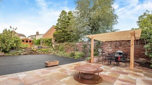 Ein Garten mit Grillplatz, einem runden Tisch und einer Pergola.