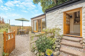Un bâtiment rustique en pierre, doté d’une porte en bois et d’un petit patio avec une table et des chaises.