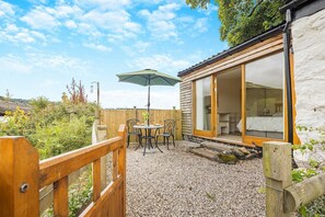 Une terrasse en bois avec une table et des chaises, un parasol et un bâtiment doté de grandes fenêtres.
