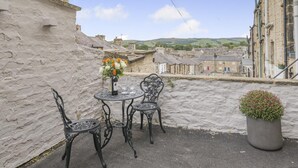A patio with a round table and chairs, a bottle of wine, and a flower arrangement. - 3 Bed in Skipton (oc-g33088) (Skipton)
