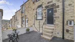 A stone building with a black door, a small outdoor seating area with a table and chairs, and a potted plant. - 3 Bed in Skipton (oc-g33088) (Skipton)