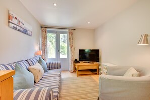 Una sala de estar con un sofá, un televisor sobre un mueble de madera, una lámpara y una ventana con cortinas.