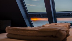 Sängyllä on siististi taitetut pyyhkeet, ja ikkunasta avautuu näkymä auringonlaskuun.