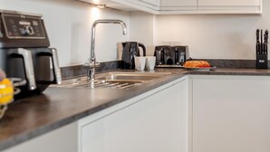 Moderni keittiö, jossa on integroitu pesuallas, kahvinkeitin, leivänpaahdin ja veitsiteline.