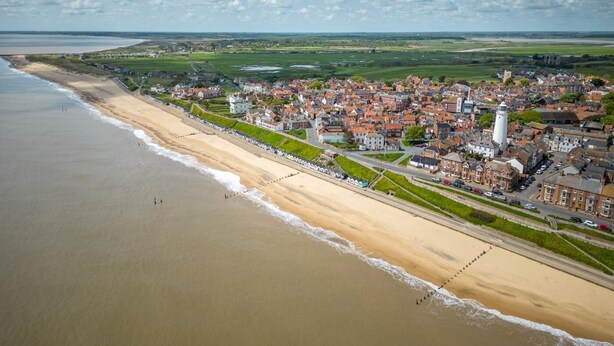 Uma cidade costeira com praia, edifícios históricos e uma torre imponente.