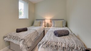 Habitación doble con dos camas, cada una con mesita de noche y lámpara, y una ventana con persianas.