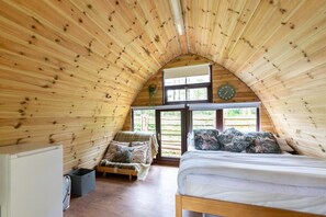 A cozy attic bedroom with wooden walls, a bed, a bench, and a small window.