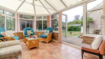 A conservatory with wicker furniture, large windows, and a view of the garden.
