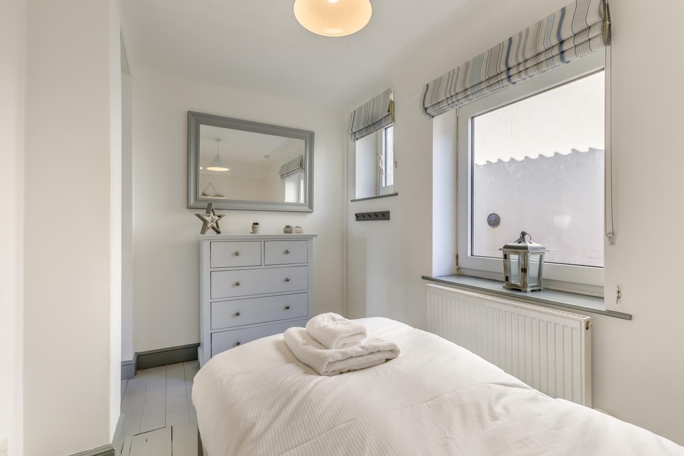 A bedroom with a bed, a dresser, a mirror, a window with blinds, and a radiator.