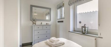 A bedroom with a bed, a dresser, a mirror, a window with blinds, and a radiator.