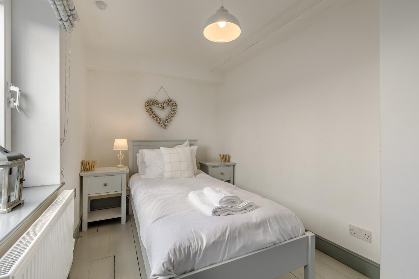 A neatly arranged bedroom with a bed, bedside tables, a lamp, and a heart-shaped wall decoration.
