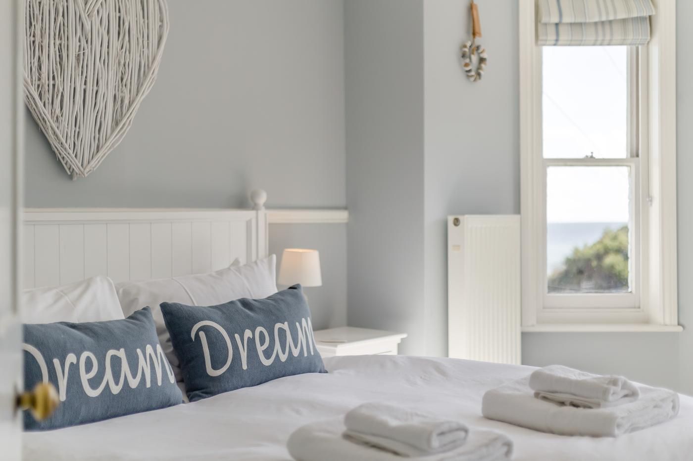 Une chambre à coucher avec un lit, des oreillers, une table de chevet avec une lampe, une fenêtre donnant sur un beau paysage et un élément décoratif en forme de cœur accroché au mur.