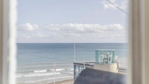 Vista do oceano por uma janela, com um edifício e um mastro de bandeira ao primeiro plano.