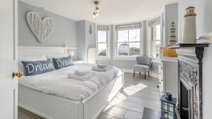 Quarto com cama grande, decoração em formato de coração na parede, lareira e vista para o exterior.