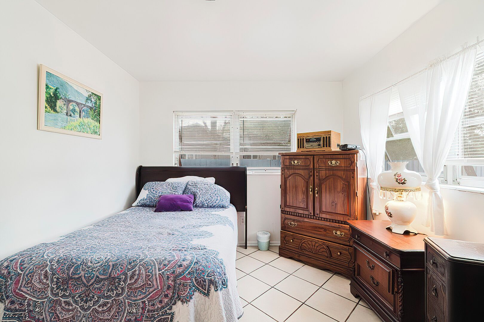 Un dormitorio con cama, cómoda, lámpara y ventana con persianas.