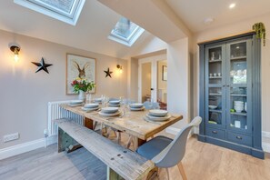 Een eetruimte met een houten tafel gedekt voor zes personen, een bank en een kast met glazen deuren.