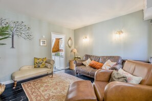 Een woonkamer met een bank, fauteuils, een salontafel en een vloerkleed. Een keuken is zichtbaar door een open doorgang.