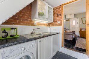 Een kleine keuken met een wasmachine, een spoelbak en een kast erboven.