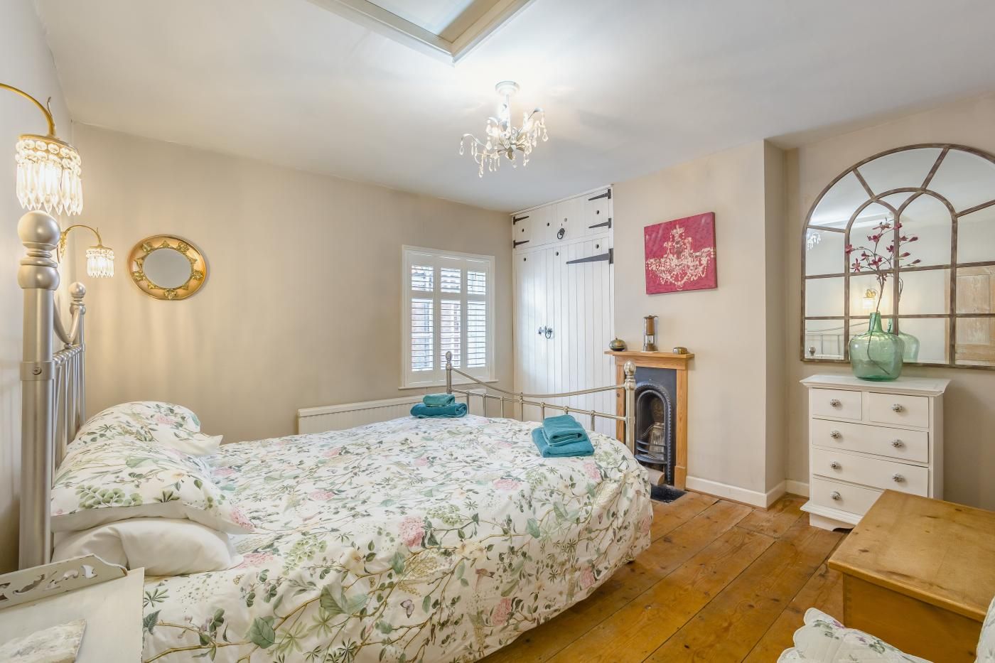 A bedroom with a bed, a dresser, a mirror, a chandelier, and a fireplace.