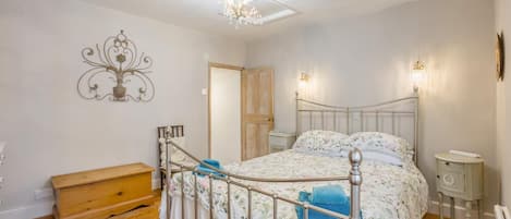 A bedroom with a metal-framed bed, wooden nightstands, a wooden bench, and a wall-mounted light fixture.