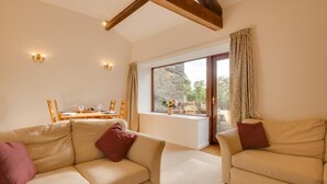 A cozy living room with two beige sofas, a wooden dining table, and a large window with curtains.