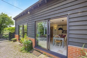 A modern house with a dining area, a kitchen, and a large sliding glass door leading to a patio. - 2 Bed in Woodbridge (oc-owls) (Ufford)