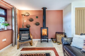 Un salon chaleureux avec une cheminée, un fauteuil, un canapé et des œuvres d’art décoratives accrochées au mur.