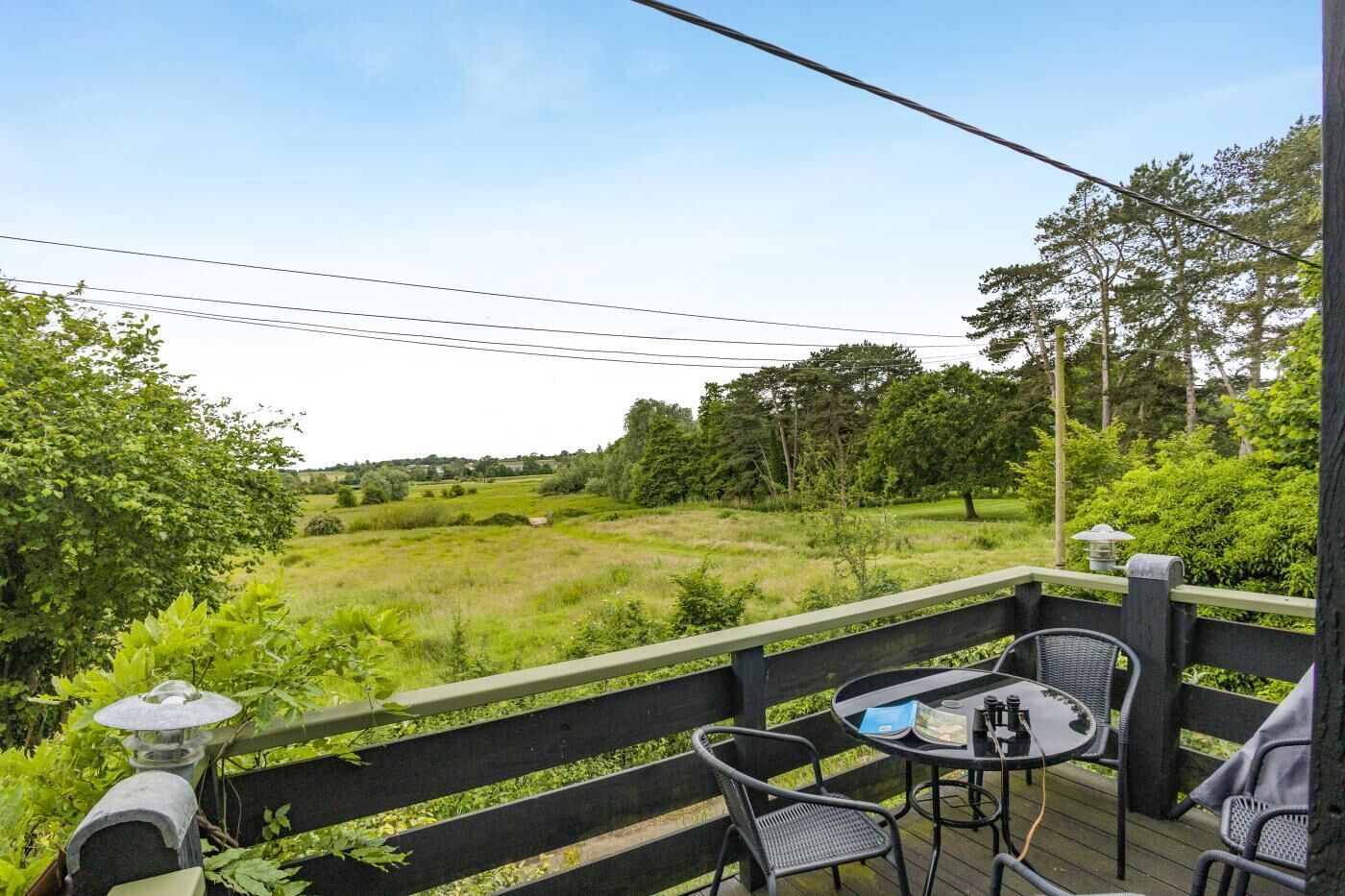 A deck with outdoor seating, a view of a grassy field, and trees in the background.