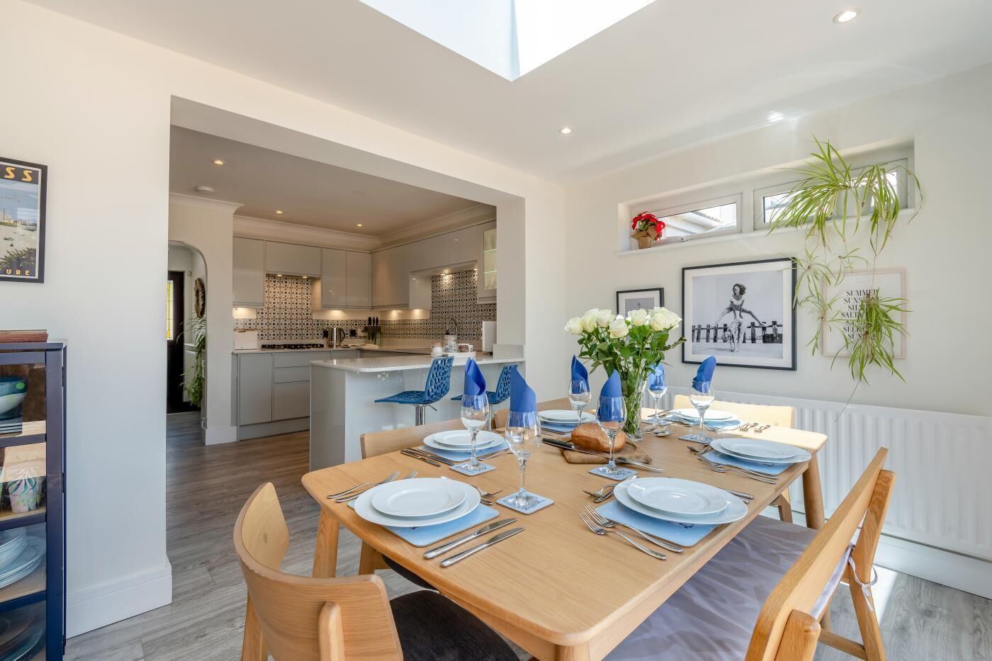Un comedor moderno con una mesa de madera para cuatro, una cocina al fondo y vista al exterior.