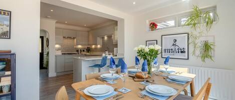 Un comedor moderno con una mesa de madera para cuatro, una cocina al fondo y vista al exterior.
