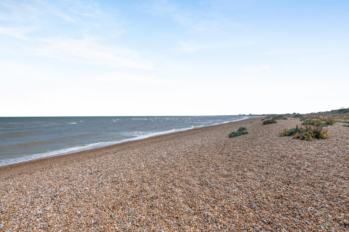 A pebbled beach with a view of the sea and distant buildings.
