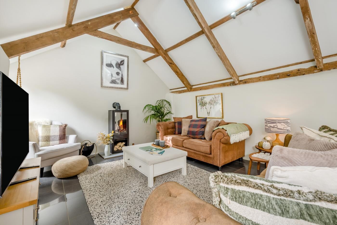 A cozy loft-style living room with exposed wooden beams, a fireplace, a sofa, a coffee table, and a television.