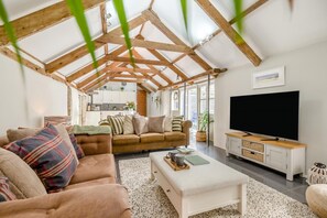 A spacious living room with a high ceiling and exposed wooden beams, a large flat-screen TV, a sofa, and a coffee table. - 1 Bed in Newquay (oc-c33290) (Quoit)