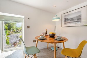A dining area with a round table, two chairs, a bowl of fruit, a bottle of wine, and a pendant light. - 1 Bed in Dolgellau (oc-bow292) (Brithdir and Llanfachreth)