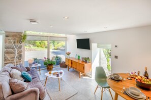 A modern living room with a sofa, coffee table, and dining area with a table set for two. - 1 Bed in Dolgellau (oc-bow292) (Brithdir and Llanfachreth)