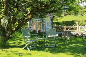 A rustic stone building with a glass door, two green chairs, and a stone wall in a lush green setting. - 1 Bed in Dolgellau (oc-bow292) (Brithdir and Llanfachreth)