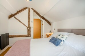 A bedroom with a sloped ceiling, a bed with white linens, a wooden headboard, and a pink throw blanket. - 1 Bed in Dolgellau (oc-bow292) (Brithdir and Llanfachreth)