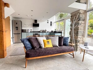 A modern living area with a sofa, a dining table, and a kitchen in the background. - 1 Bed in Dolgellau (oc-bow292) (Brithdir and Llanfachreth)