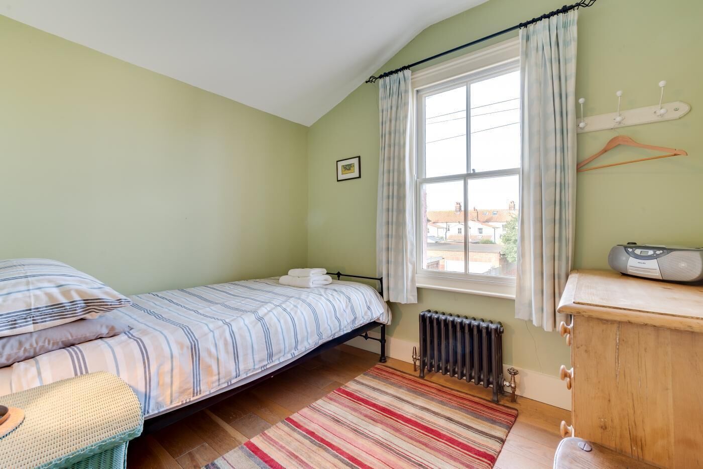 A small, cozy bedroom with a single bed, a wooden dresser, a radiator, and a window with curtains.